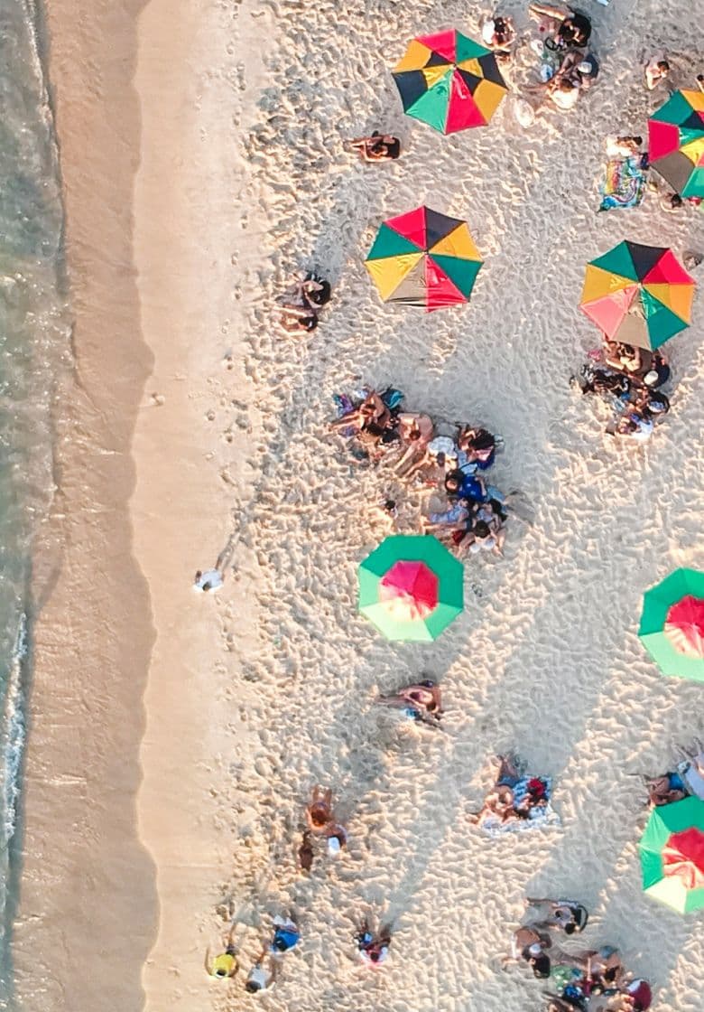 Bird's eye view of sandy beach with holidaymakers sunbathing and playing in the sea