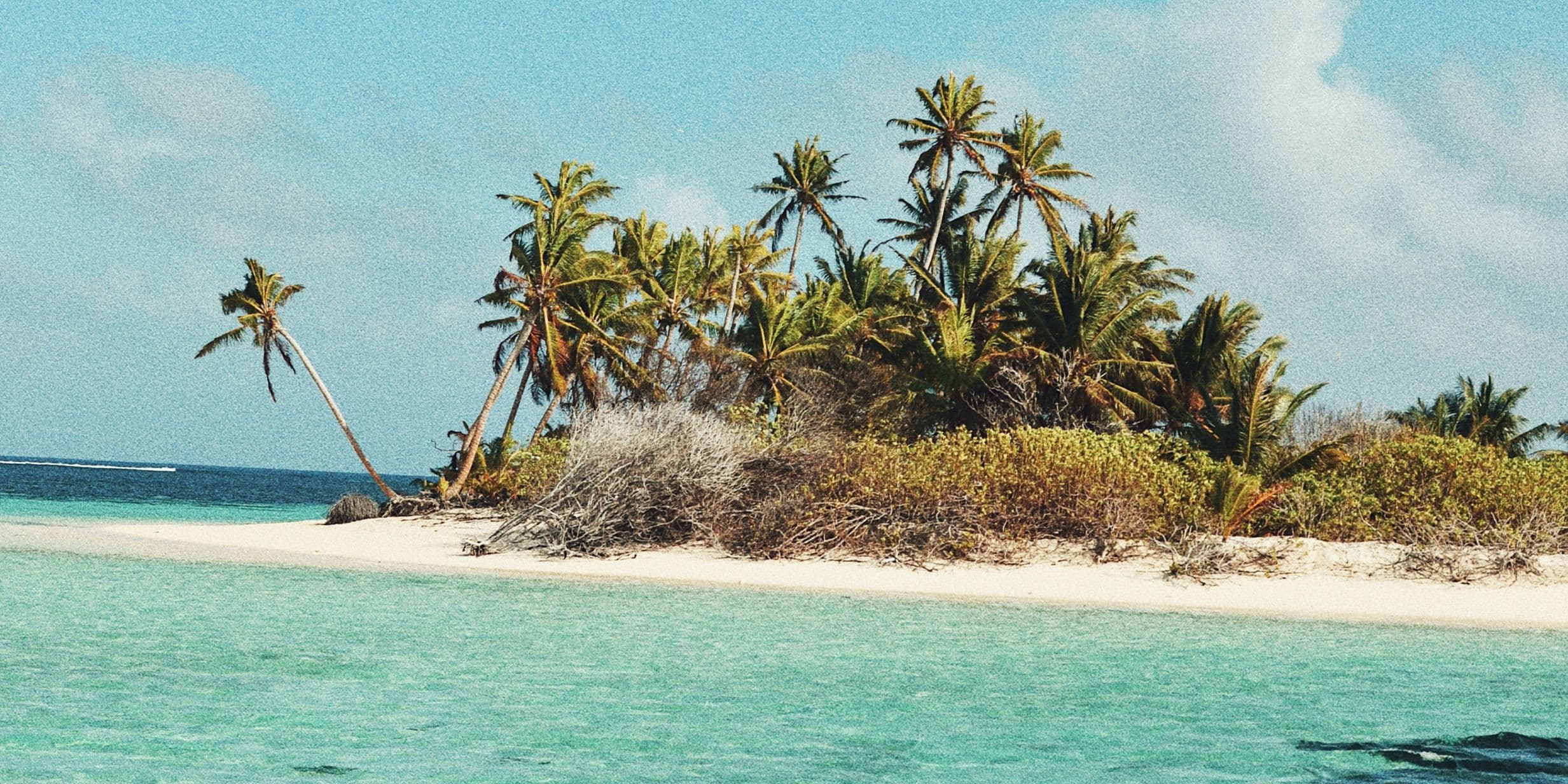 Small tropical island with white sandy beach, turquoise water and leaning palm trees.