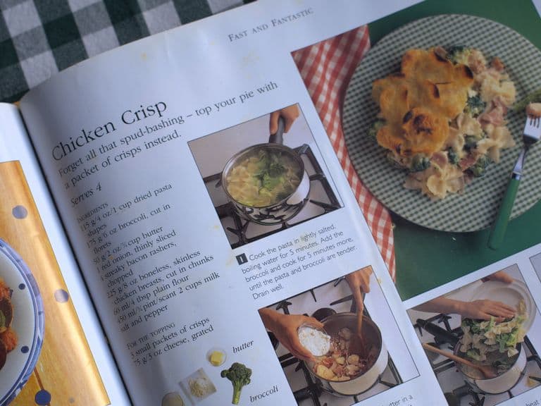Open cookbook showing a chicken crisp recipe with steps and photos on a checkered tablecloth.