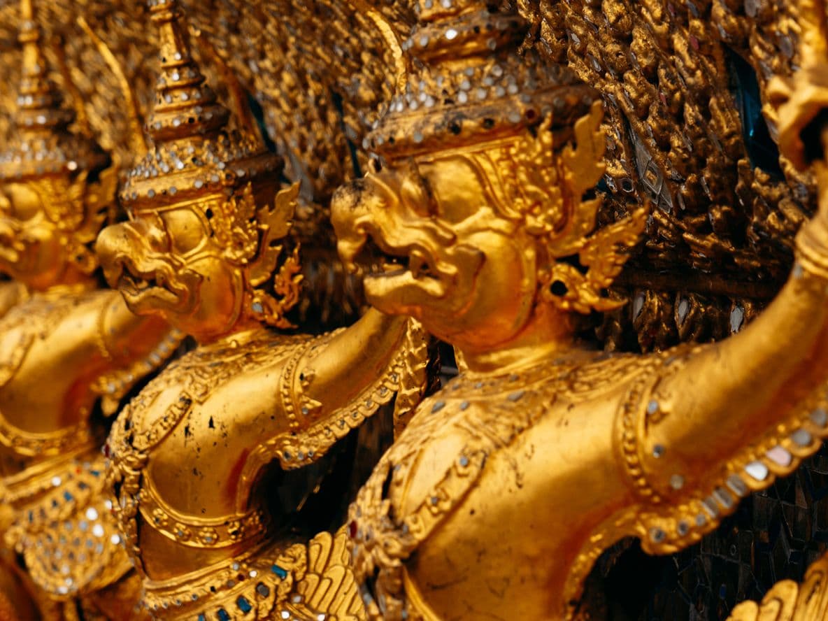 Close-up of gilded mythic guardian figures with ornate crowns and jewelry carved in a row on a temple facade.