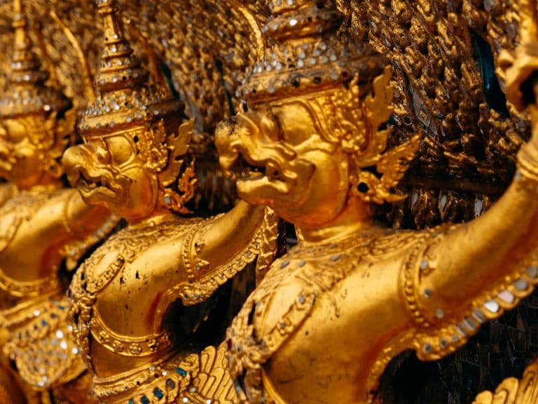 Close-up of gilded mythic guardian figures with ornate crowns and jewelry carved in a row on a temple facade.