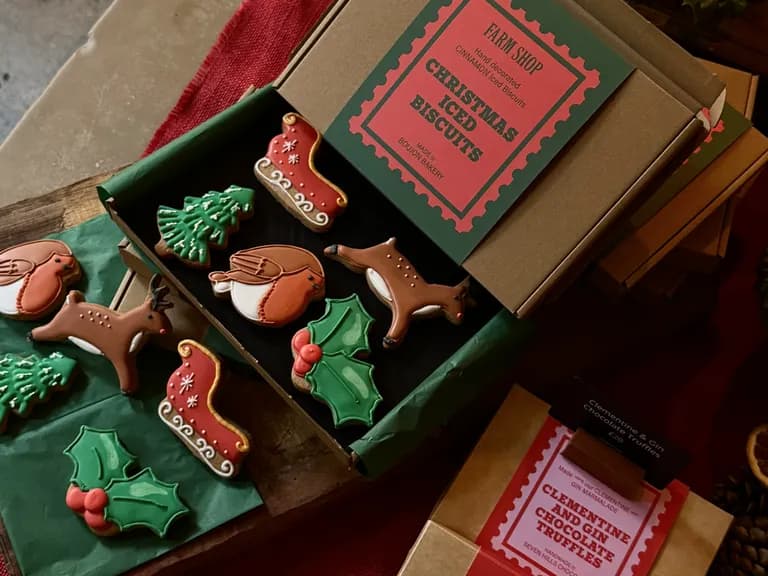 Holiday-themed iced biscuits, including reindeer, robins, holly, and Christmas trees, arranged in an open box with festive packaging.