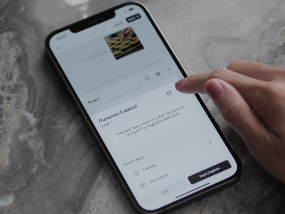 Hand interacting with a smartphone on a marble surface, displaying a caption generation app. A glass of water is nearby.
