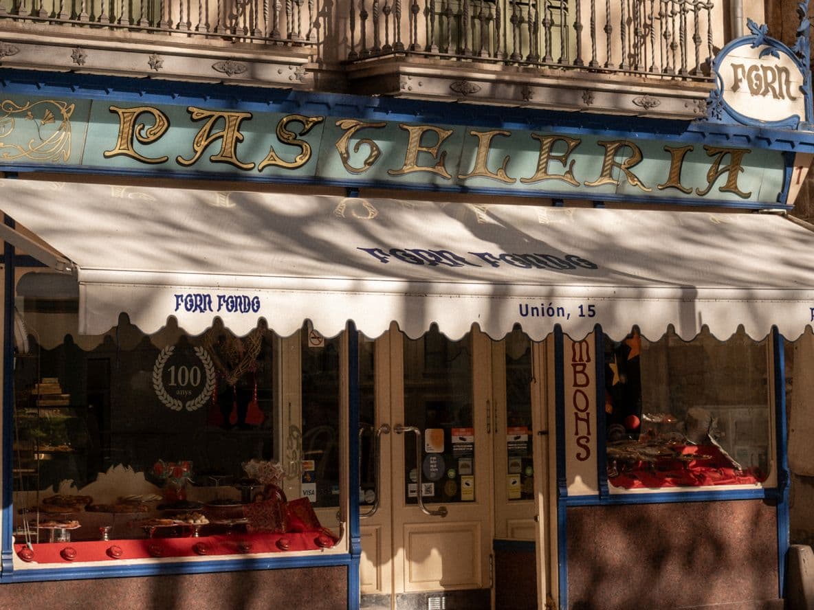 Historic pastry shop with a white awning and blue accents, displaying pastries in the window and classic signage above the entrance.