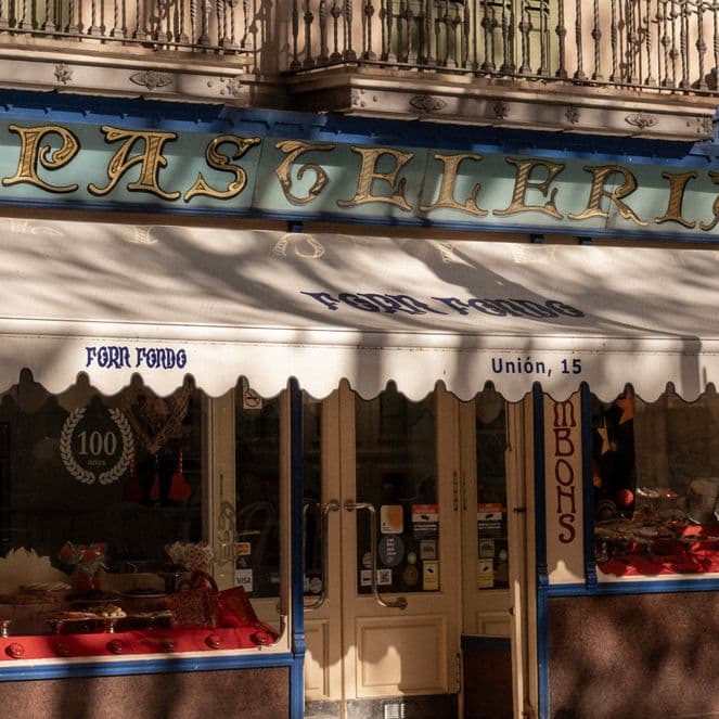 Historic pastry shop with a white awning and blue accents, displaying pastries in the window and classic signage above the entrance.