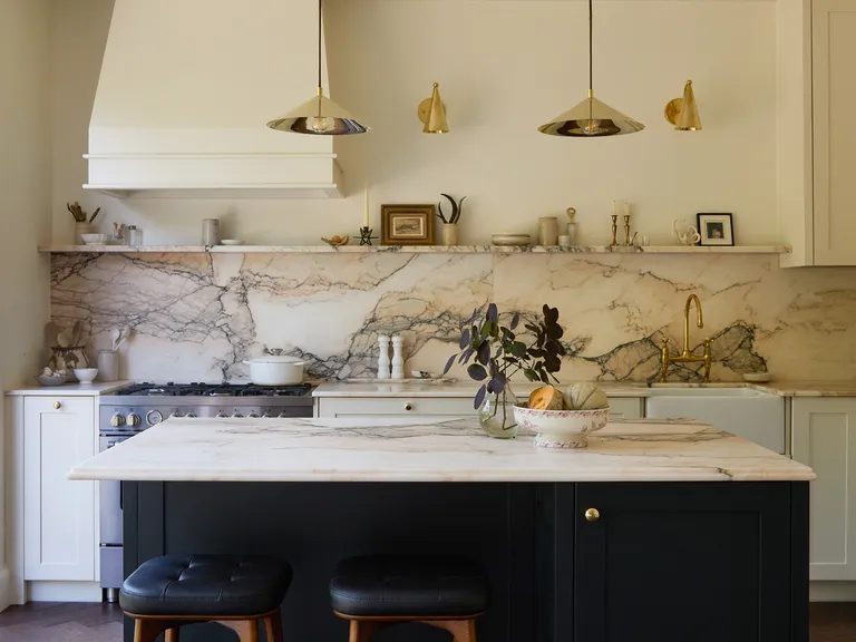 Elegant kitchen with marble countertops, white cabinets, black island, pendant lights, and large window. Decor includes plant and small frames.