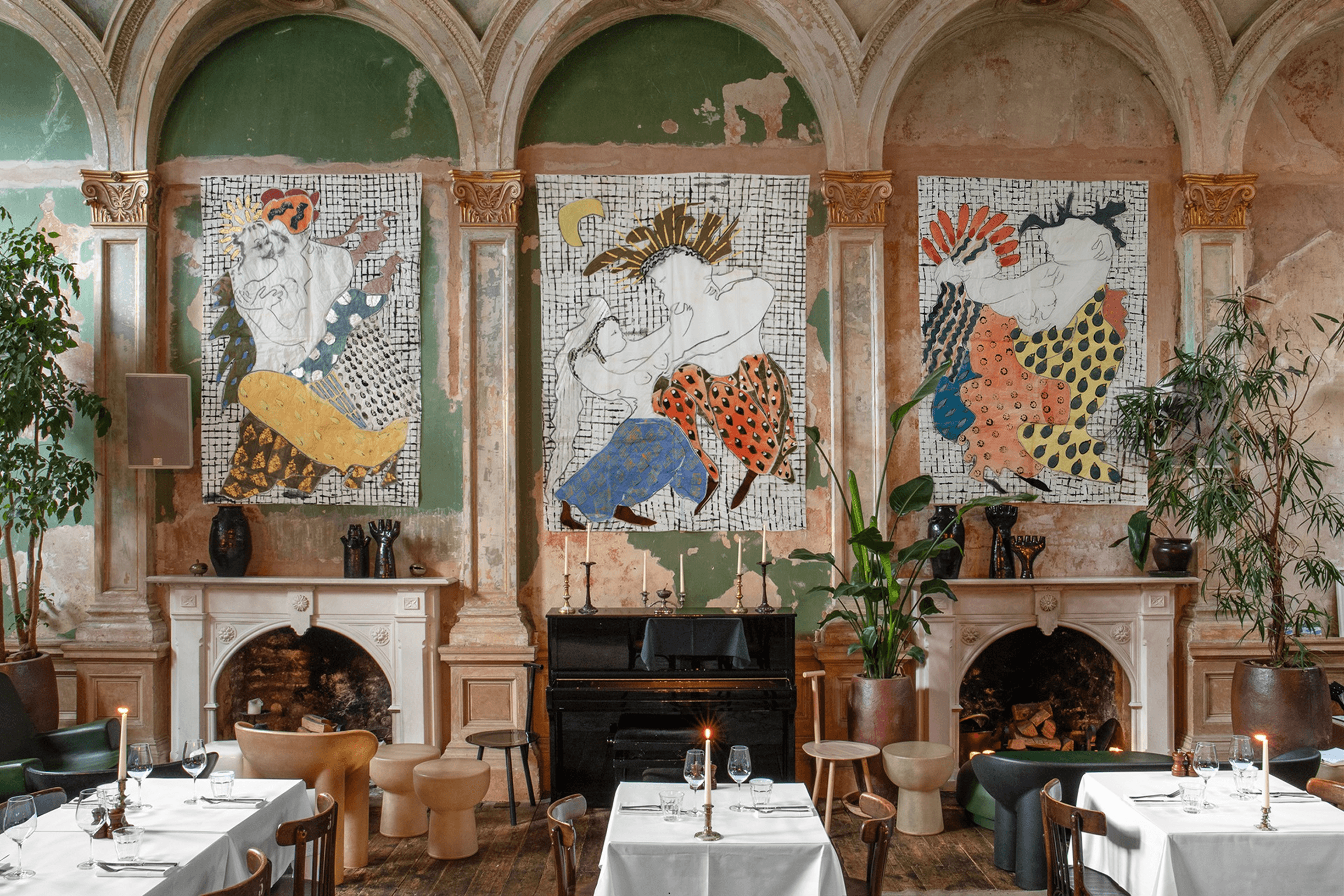 Elegant restaurant interior with arched ceilings, three vibrant abstract paintings above two fireplaces, and tables set with white linens and candles.