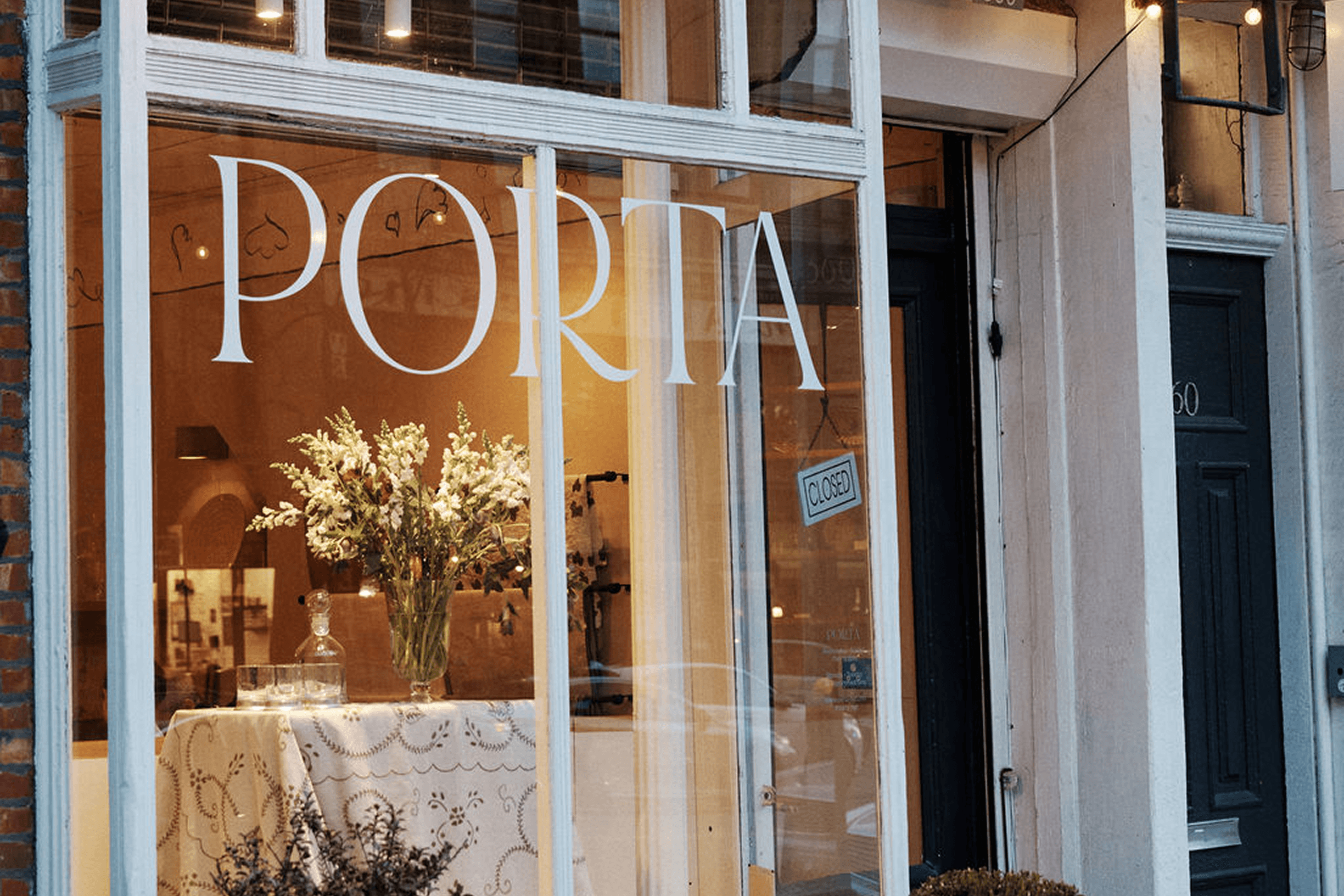 Storefront with "PORTA" on the window, displaying a vase of flowers on a table and a "Closed" sign on the door.