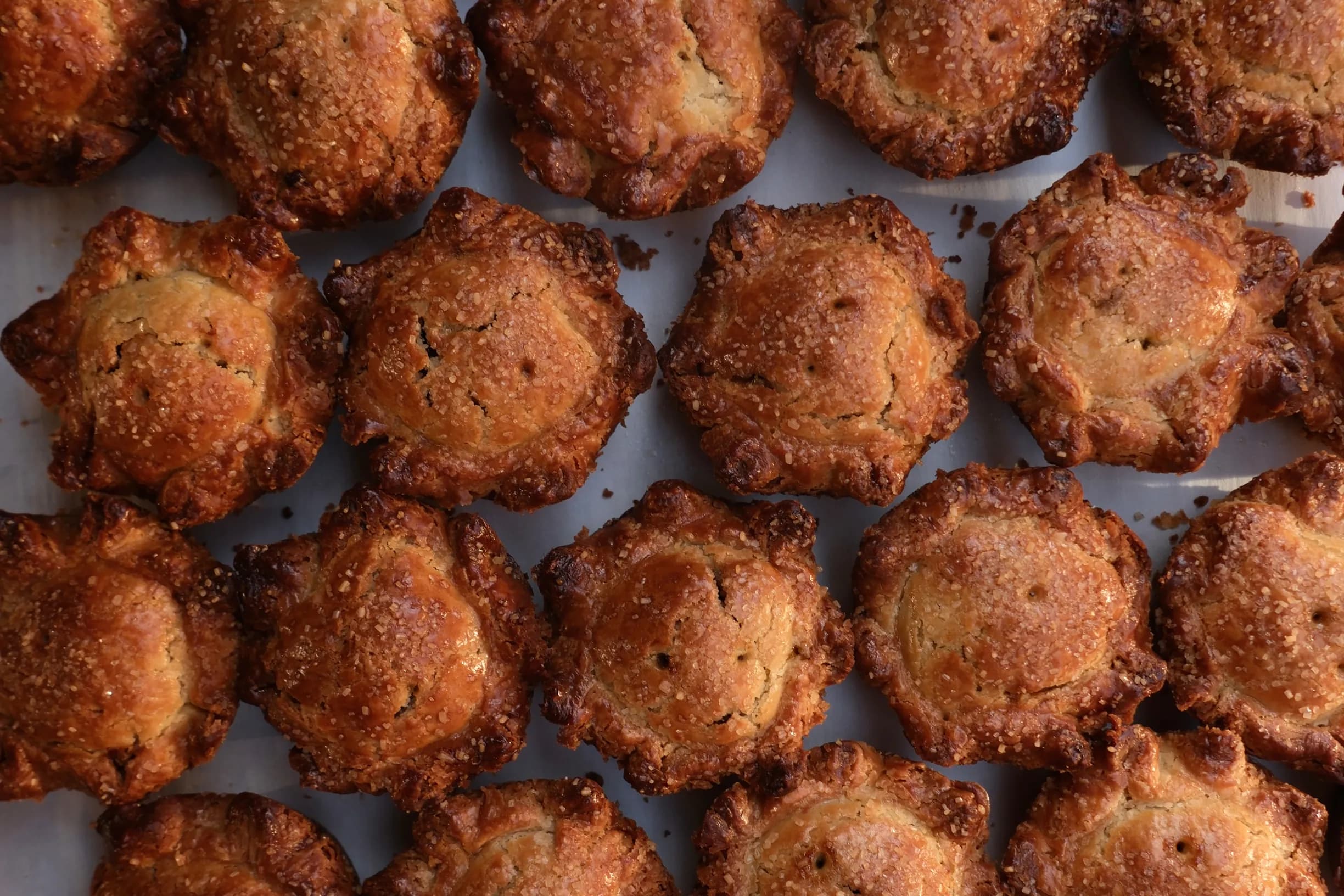 Rows of golden-brown, flaky pastries topped with coarse sugar, arranged on a baking sheet.