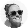 Smiling person wearing sunglasses, hair in a bun, and looking upward against a white background. Black and white photo.