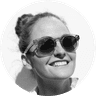 Smiling person wearing sunglasses, hair in a bun, and looking upward against a white background. Black and white photo.