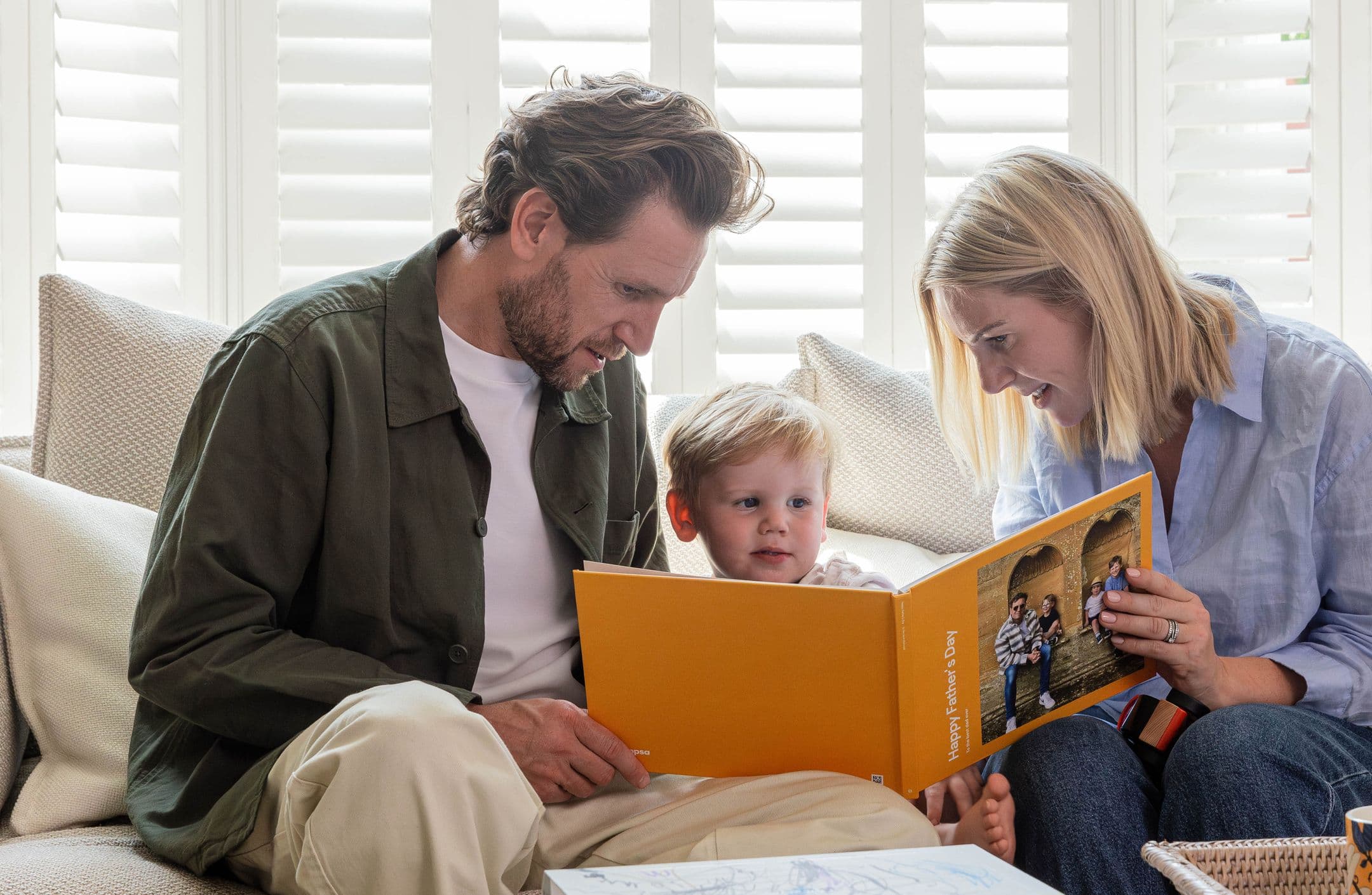 A mother and young child present the child's father with a Father's Day-themed Photo Book