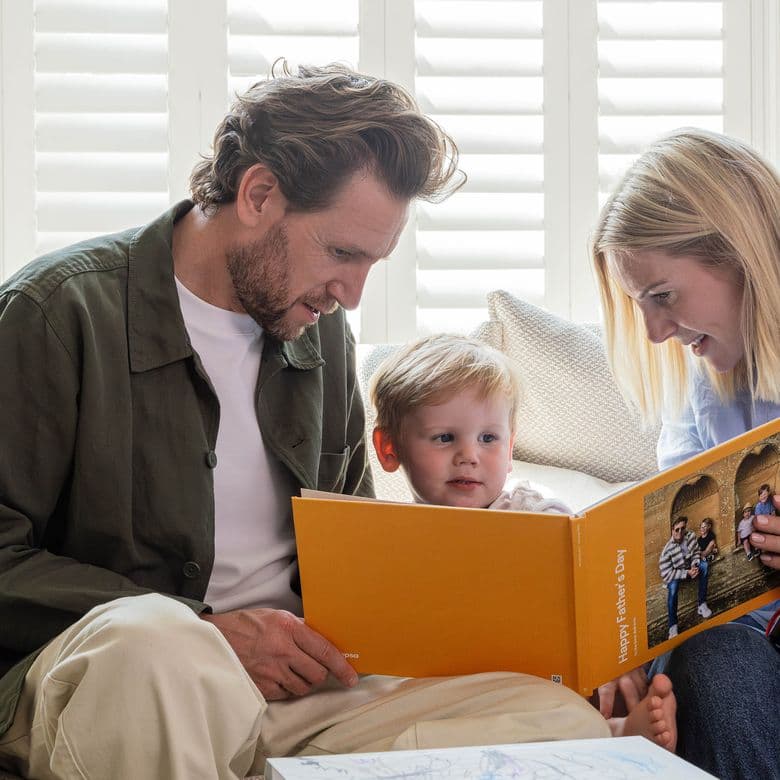 A mother and young child present the child's father with a Father's Day-themed Photo Book