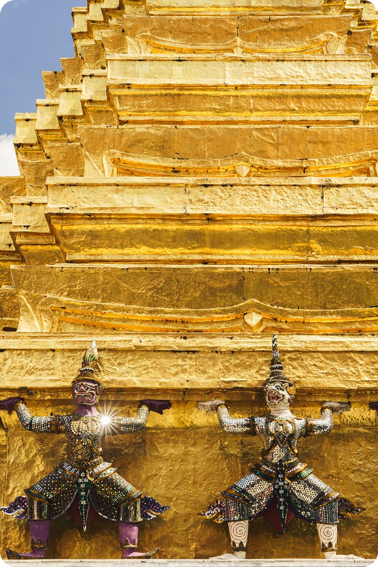 Gilded tiered temple wall with two jeweled guardian statues appearing to hold up the golden structure.