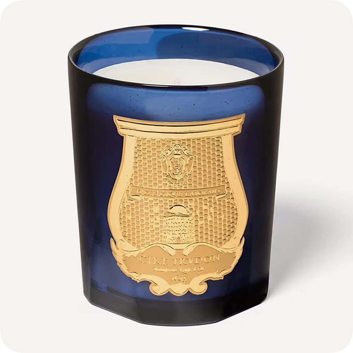 Blue glass candle with a gold emblem on the front, featuring intricate details and text.