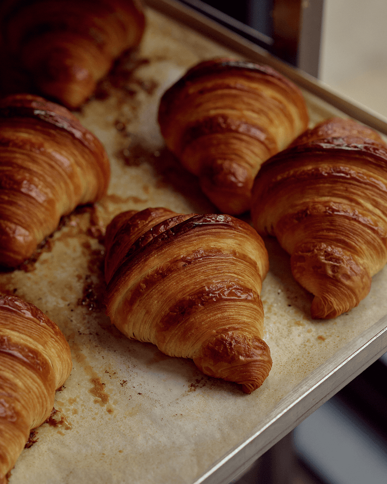 Freshly baked croissants on a baking tray, with a golden-brown, crispy texture.