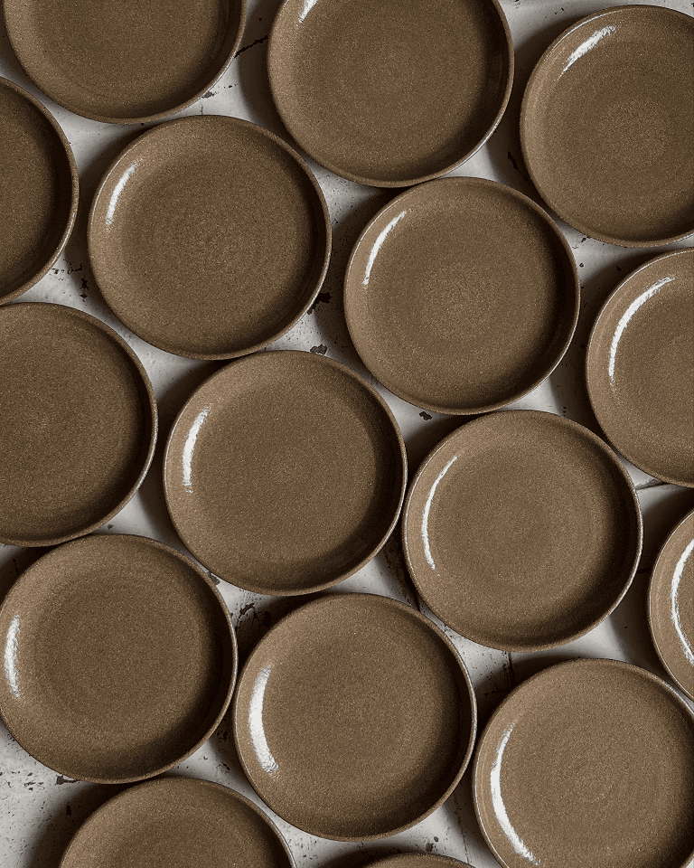 Multiple brown ceramic plates arranged closely on a white surface with black splatters.