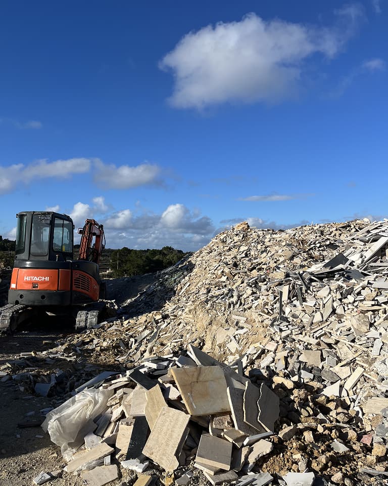A Hitachi excavator near a large pile of rubble and broken tiles under a clear blue sky.