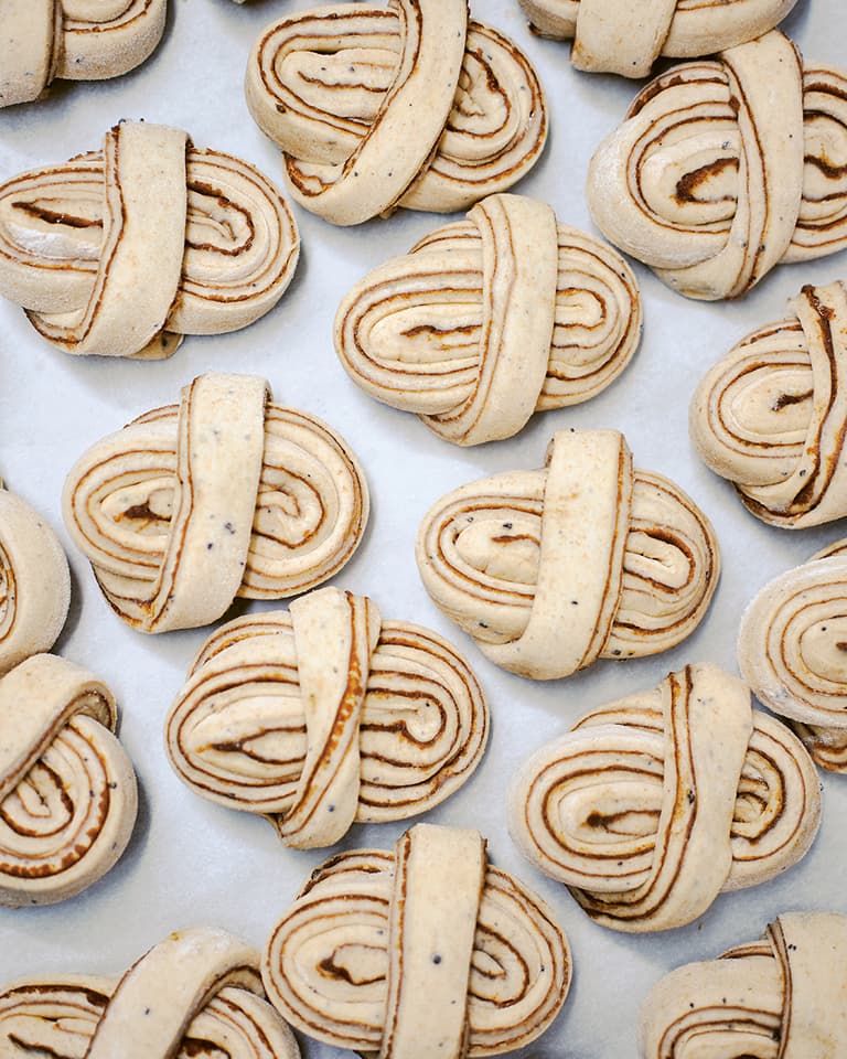 Several intricately shaped dough pieces, resembling knots, are arranged on a baking sheet, showcasing layers of dough and spices.