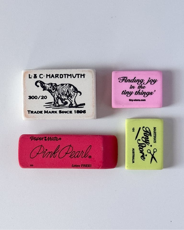 Four rectangular erasers—white, light pink, hot pink, and lime—arranged in a grid on a white background, each with printed logos and text.