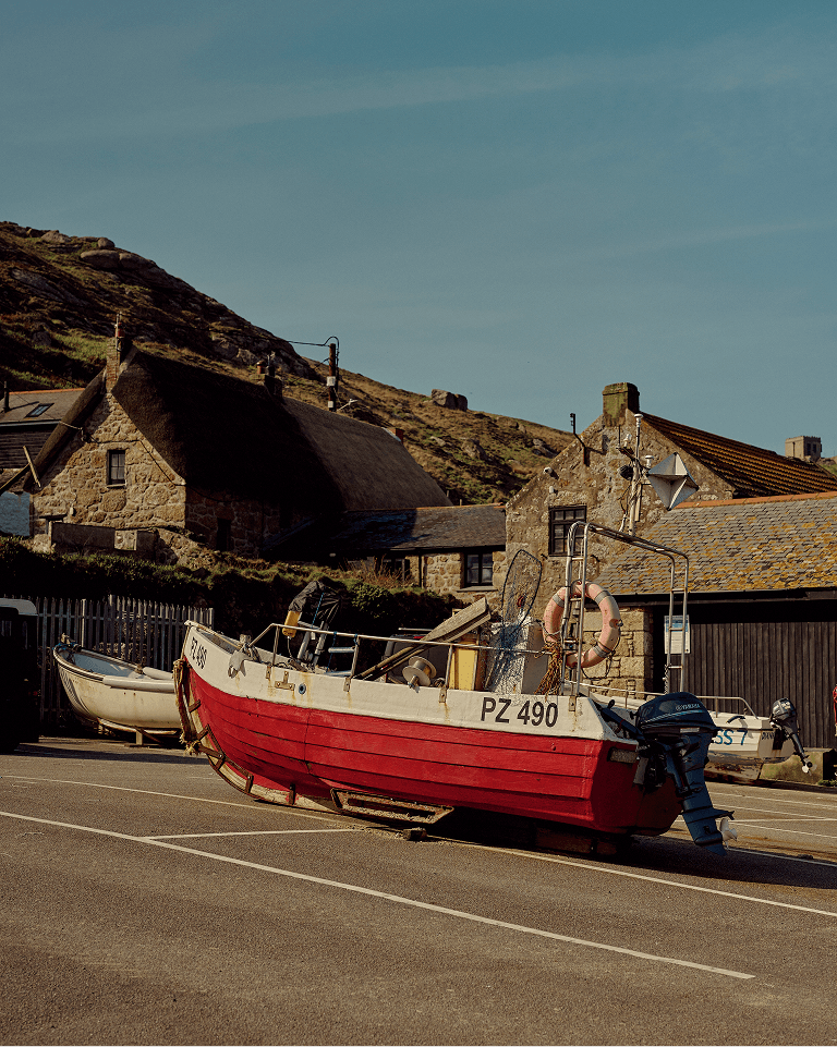 A red and white boat labeled PZ 490 is parked on a street with quaint stone buildings and hills in the background under a clear blue sky.