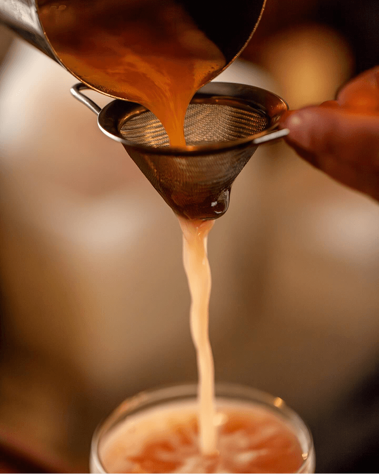 Orange liquid being poured through a fine mesh strainer into a glass.