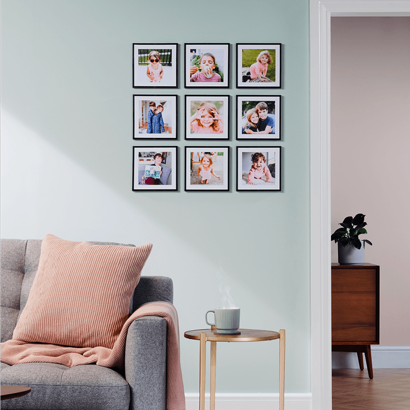 A cozy living room with nine Popsa photo tiles arranged in a grid on a pale green wall