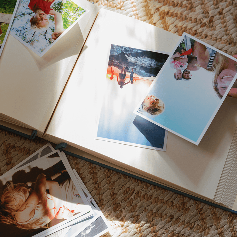 Open photo album with scattered colourful photos of a family on a textured surface