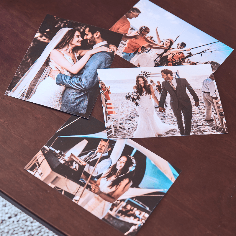 Four wedding photos on a wooden table, showing a couple embracing, walking on a beach, celebrating with friends, and dancing.