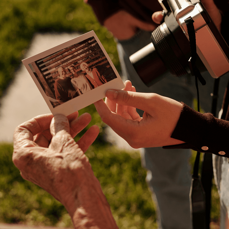 Hands holding an instant photo of two people, with a vintage camera visible in the background