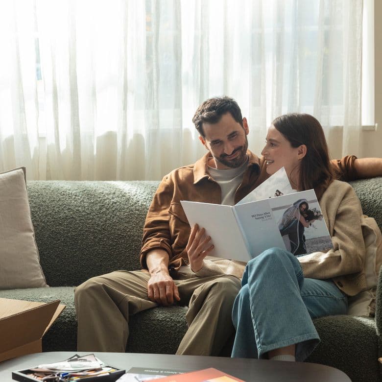 A married couple sitting on a sofa looking back at their wedding photos in an anniversary photo book