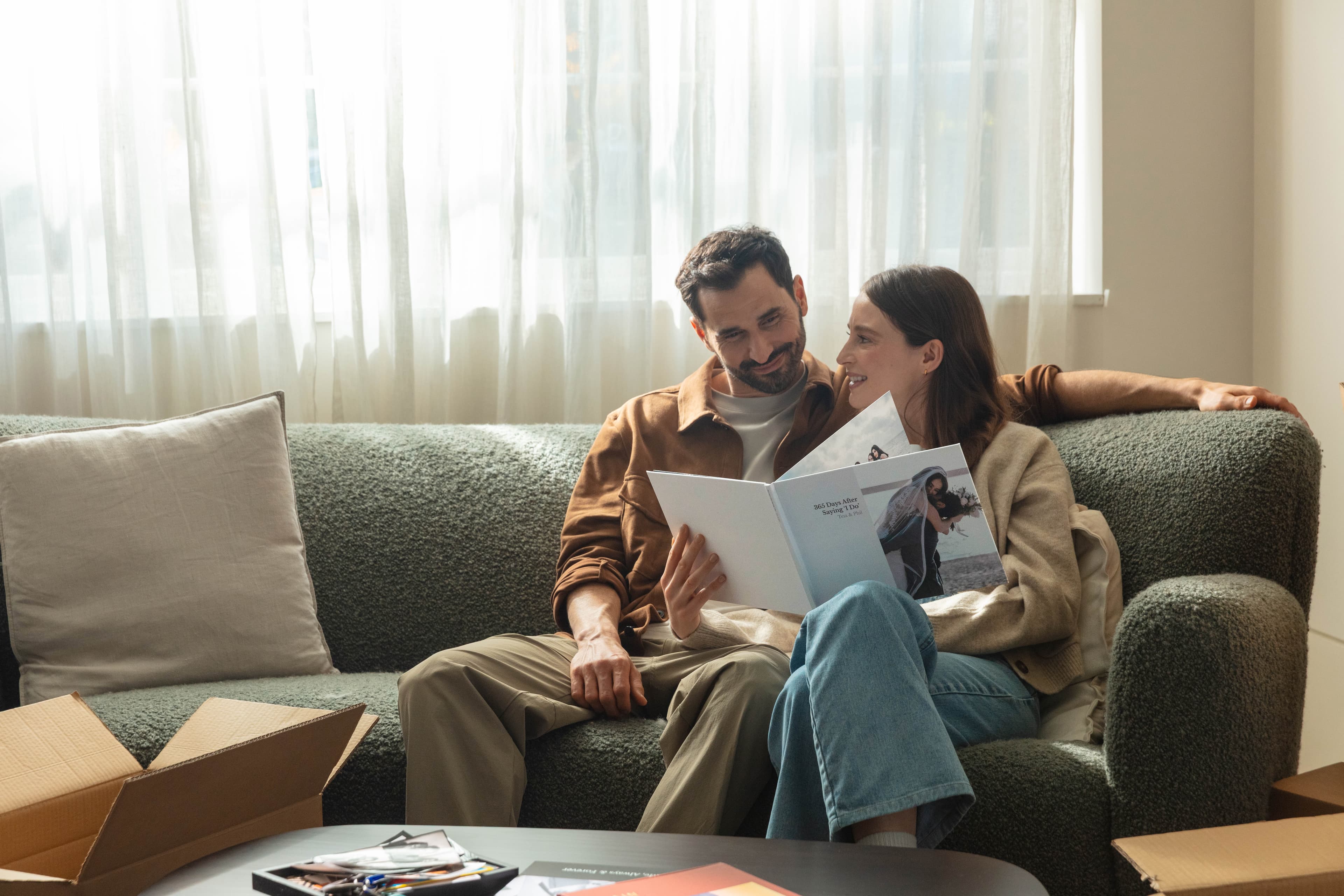 A married couple sitting on a sofa looking back at their wedding photos in an anniversary photo book