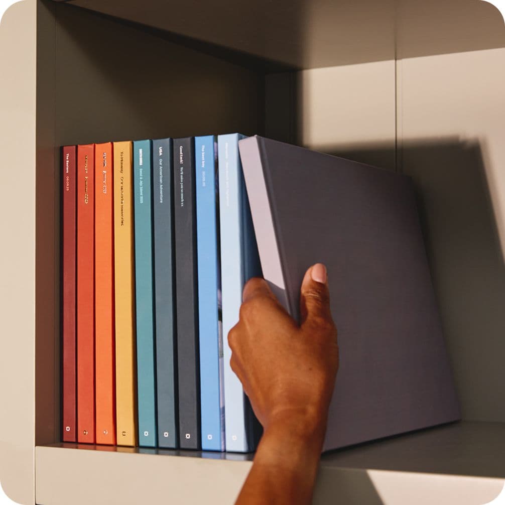 Hand pulling a gray book from a shelf with colorful books lined up in a gradient from red to blue.