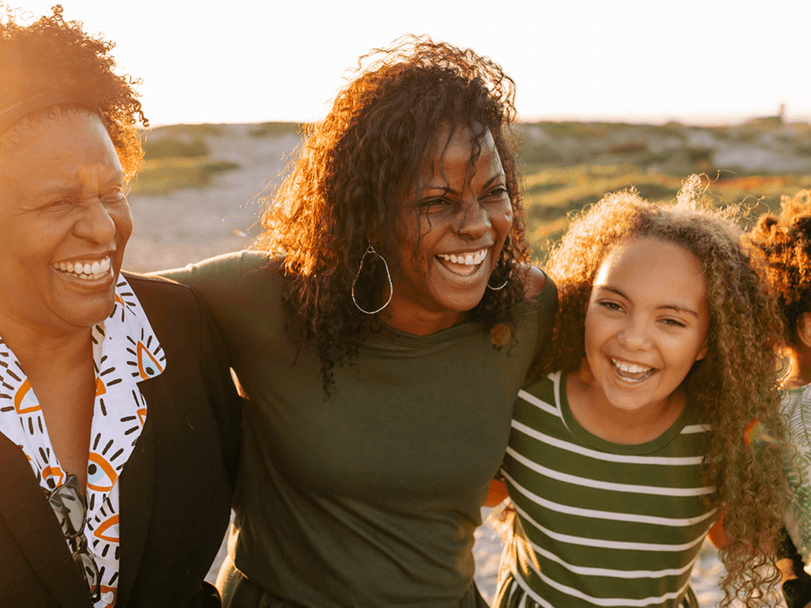 A mother, daughter and grandma smiling and hugging in a park setting