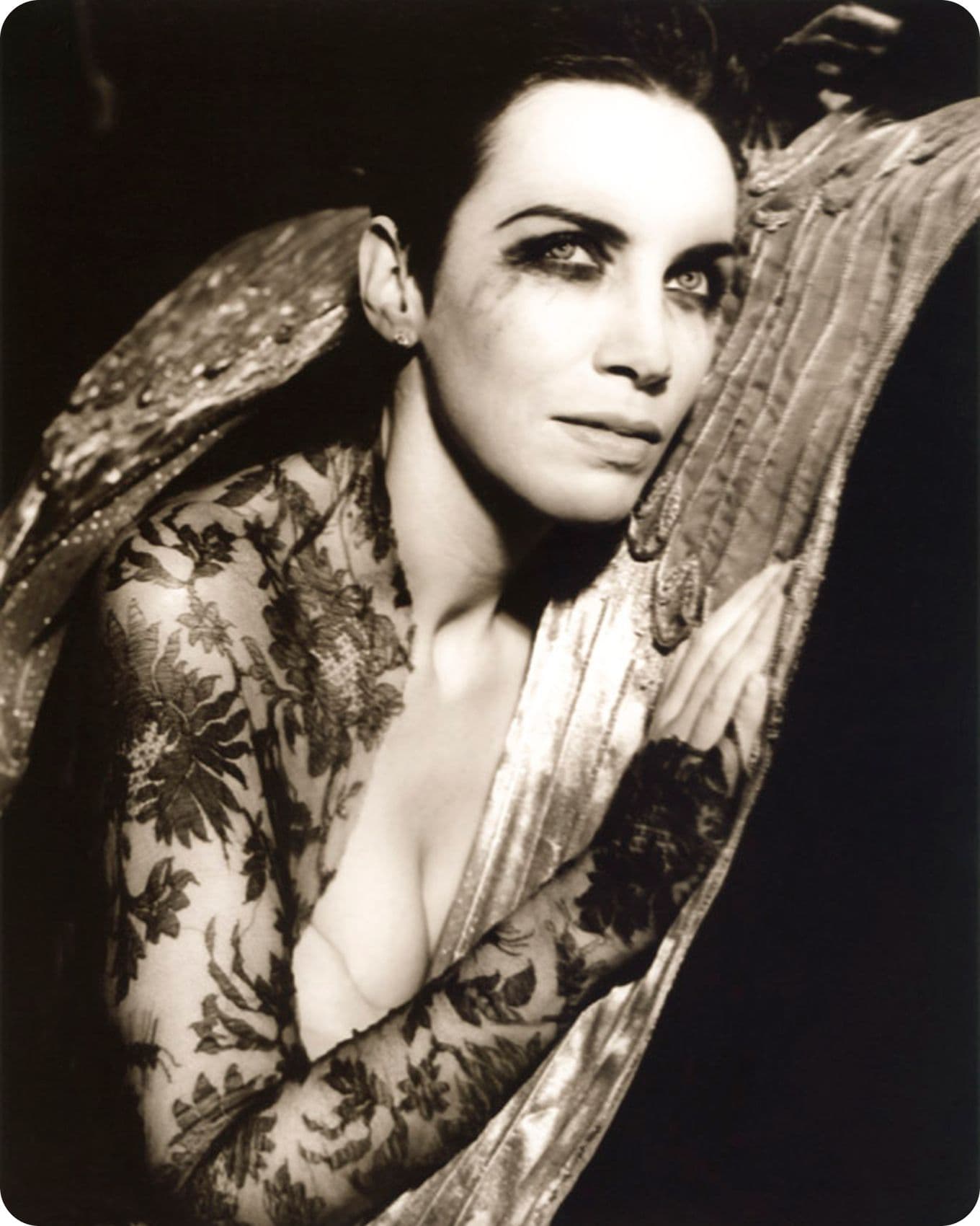 Annie Lennox with floral body paint and dramatic makeup, leaning on a textured surface, in a black and white photograph.