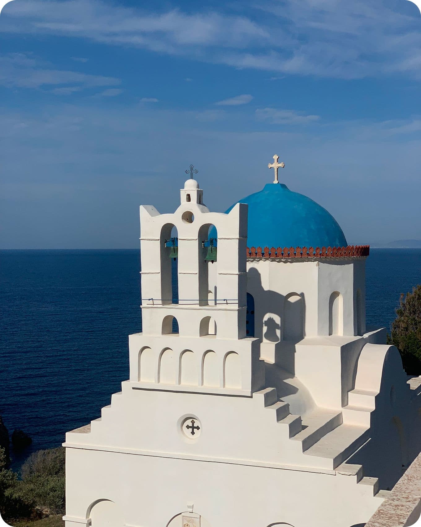 White church with a blue dome and cross overlooking the sea under a clear sky.