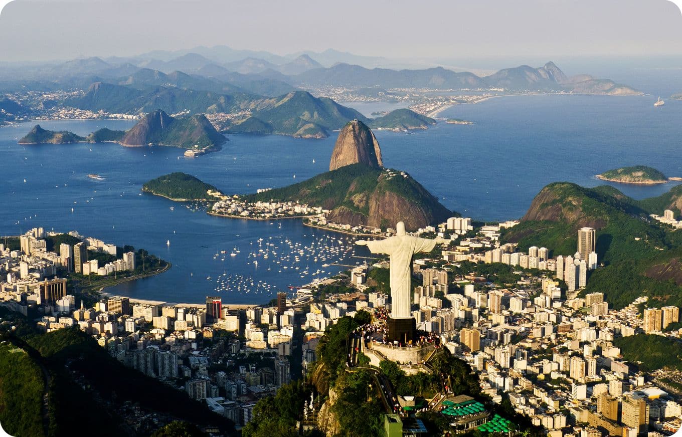Aerial view of Rio de Janeiro with Christ the Redeemer statue, Sugarloaf Mountain, and surrounding cityscape by the ocean.
