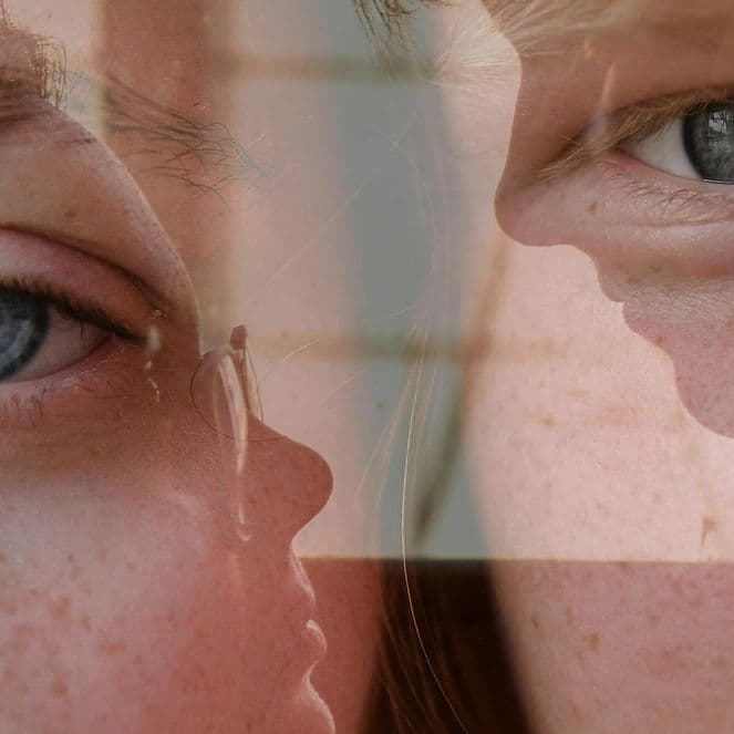 Close-up of a person's blue eyes and face, with a reflective overlay creating a layered effect.
