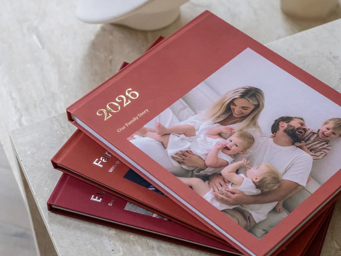 A stack of red photobooks on a table, with a family photo and the year 2026 on the cover.