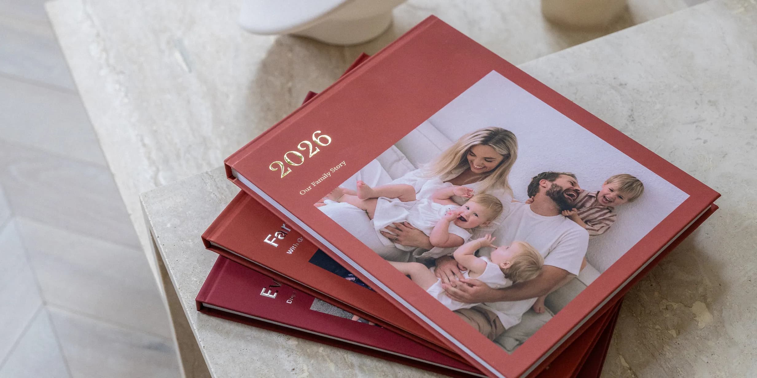 A stack of red photobooks on a table, with a family photo and the year 2026 on the cover.