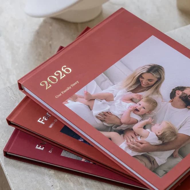 A stack of red photobooks on a table, with a family photo and the year 2026 on the cover.