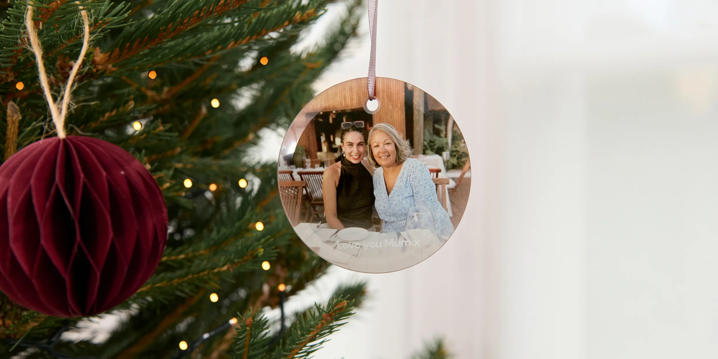 A Christmas tree decorated with a maroon ornament and a round photo ornament featuring two people with the text "Love you Mum x."
