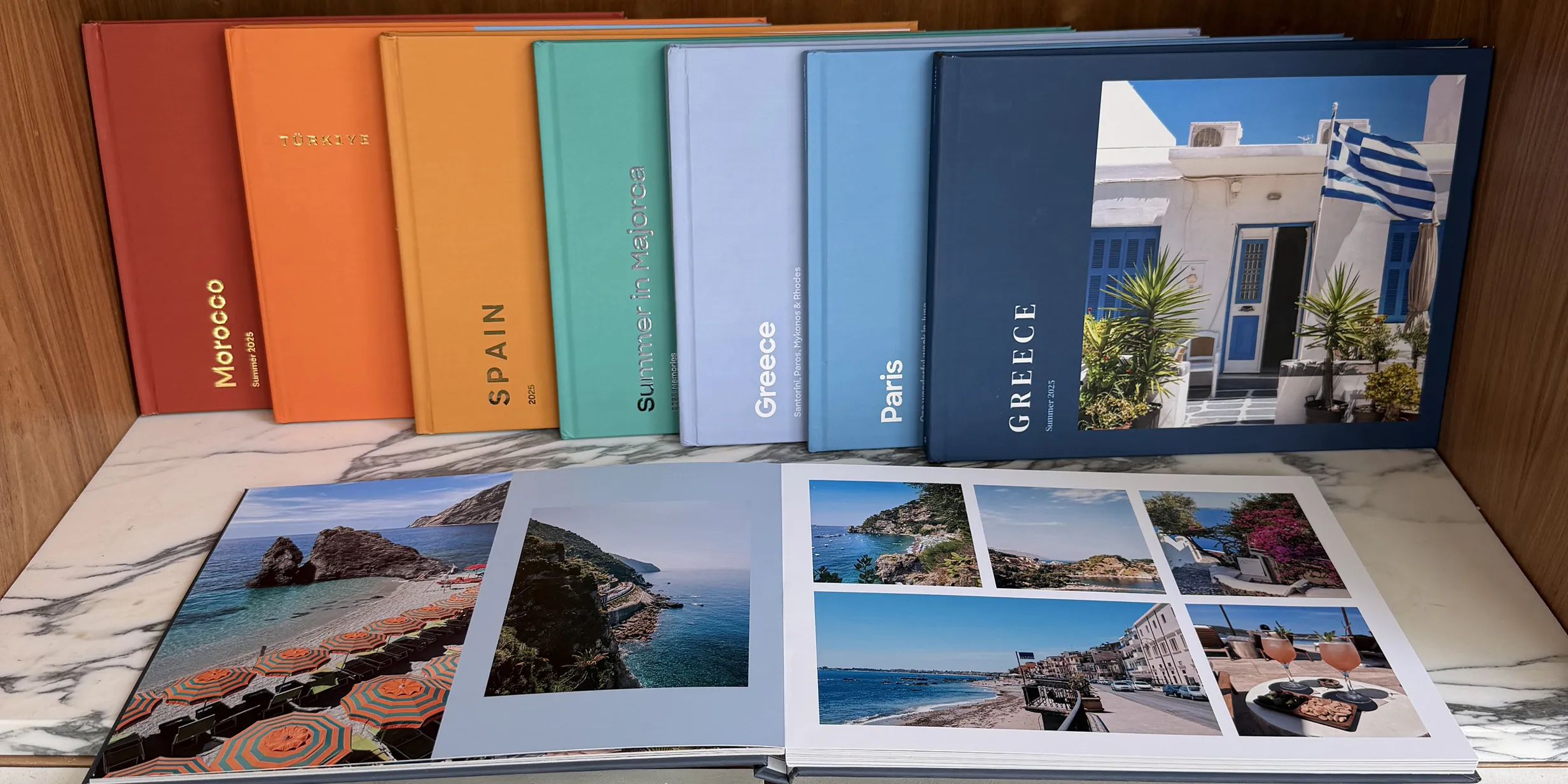 Colorful travel photo albums, including Morocco, Spain, and Greece, on a shelf. One open album displays vibrant beach scenes and coastal views.