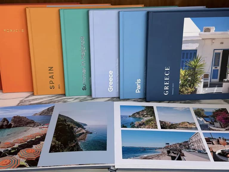 Colorful travel photo albums, including Morocco, Spain, and Greece, on a shelf. One open album displays vibrant beach scenes and coastal views.