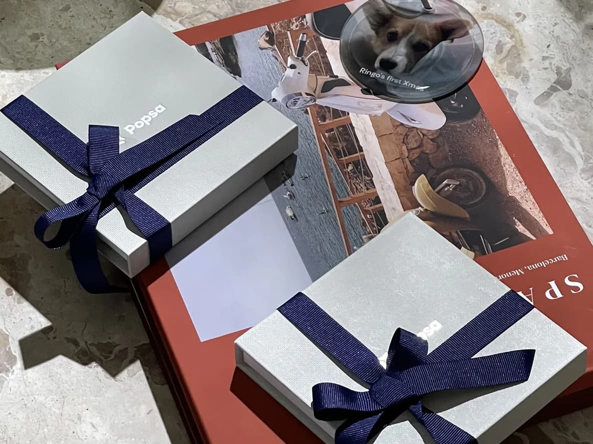 Two gift boxes with navy ribbons on a red book and a coaster with a dog photo on a marble surface.
