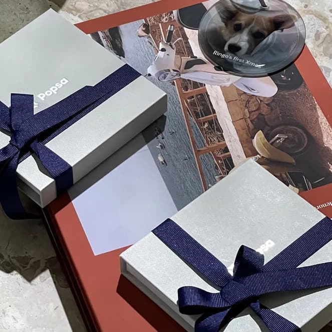 Two gift boxes with navy ribbons on a red book and a coaster with a dog photo on a marble surface.