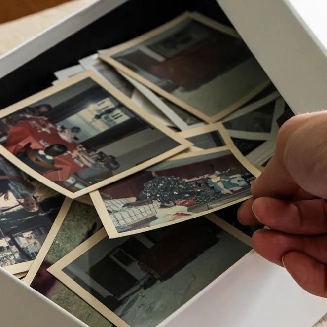 A hand sorting through a box of vintage photographs on a table, featuring various moments and memories.