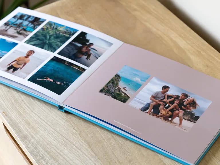 Open photo album on wood, showcasing beach vacation photos: a laughing family on sand, tropical landscapes, a child in water, and a swimmer.