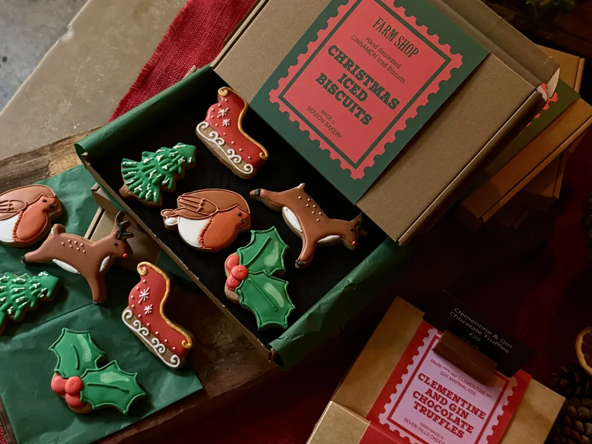 Holiday-themed iced biscuits, including reindeer, robins, holly, and Christmas trees, arranged in an open box with festive packaging.