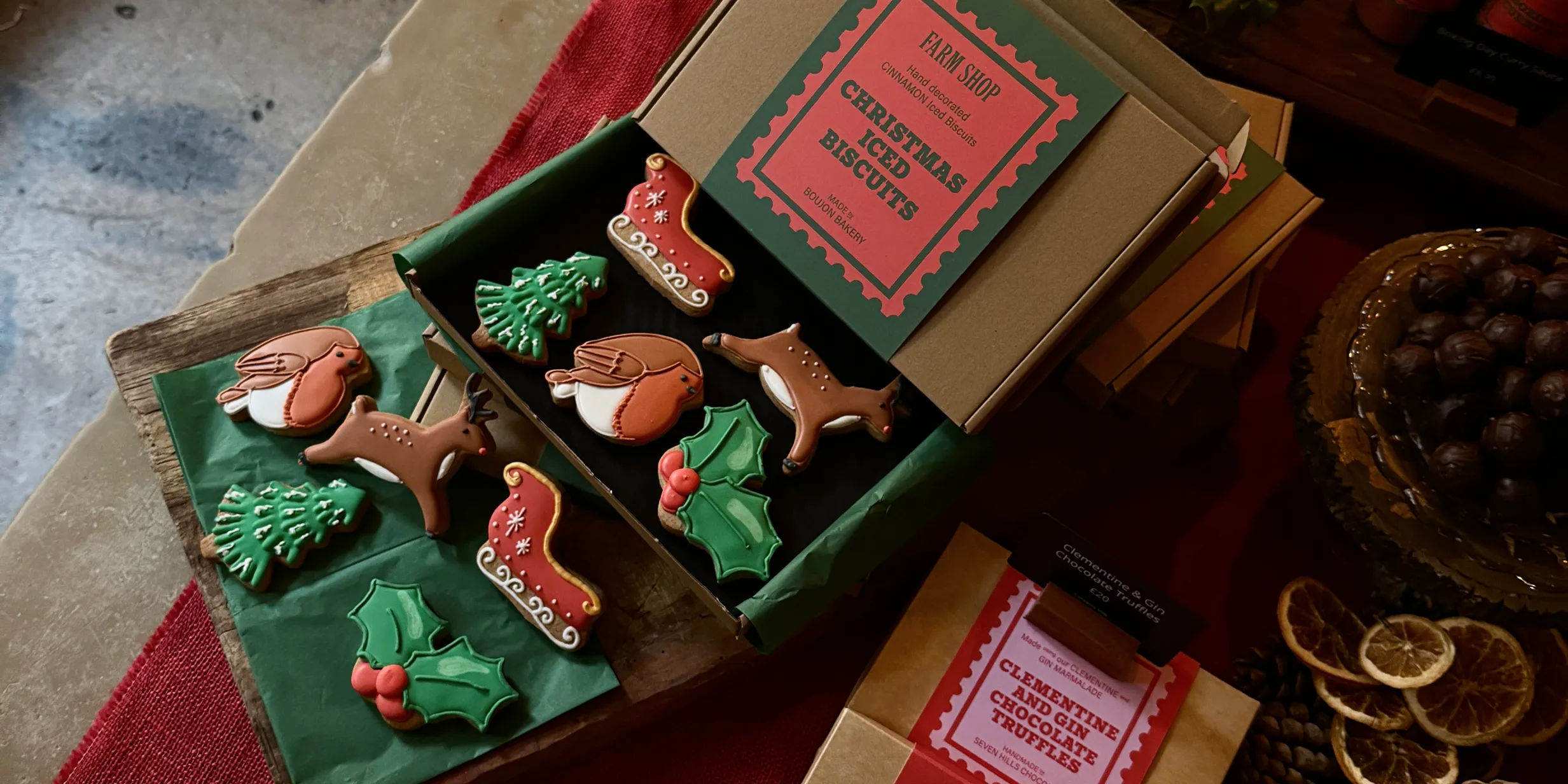 Holiday-themed iced biscuits, including reindeer, robins, holly, and Christmas trees, arranged in an open box with festive packaging.